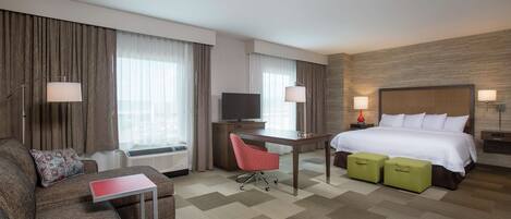 A hotel room with a bed, a desk, a chair, a sofa, and a television.