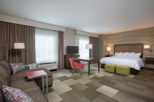 A hotel room with a bed, a desk, a chair, a sofa, and a television.