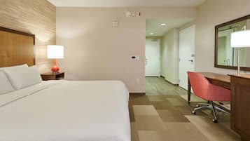 A hotel room with a bed, a desk, a chair, a lamp, and a mirror.