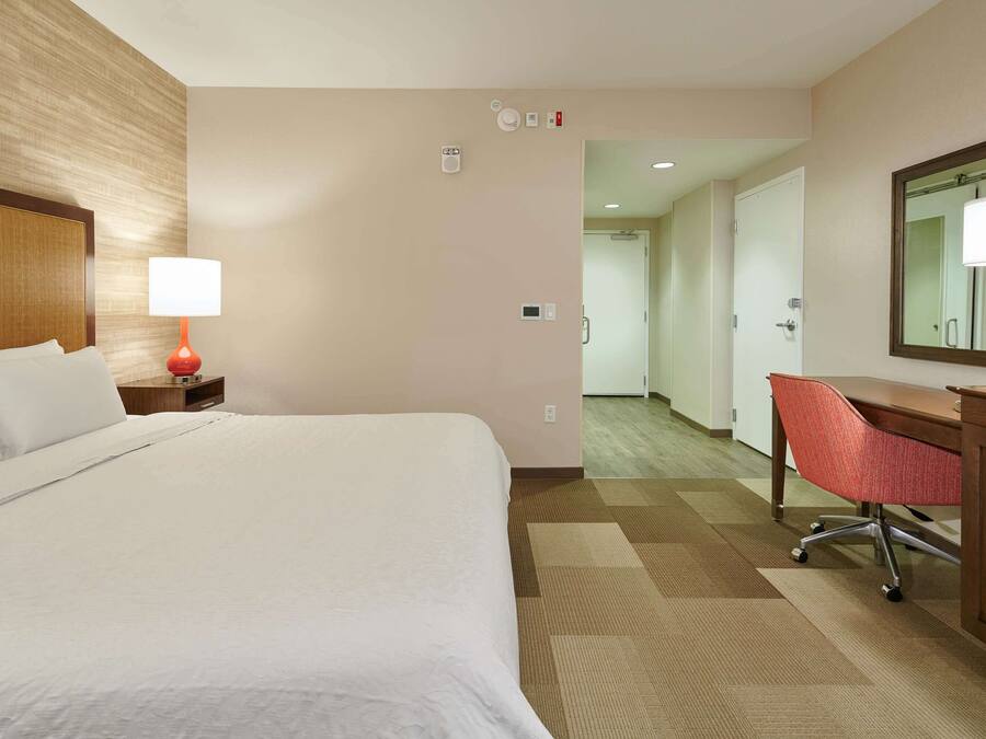 A hotel room with a bed, a desk, a chair, a lamp, and a mirror.