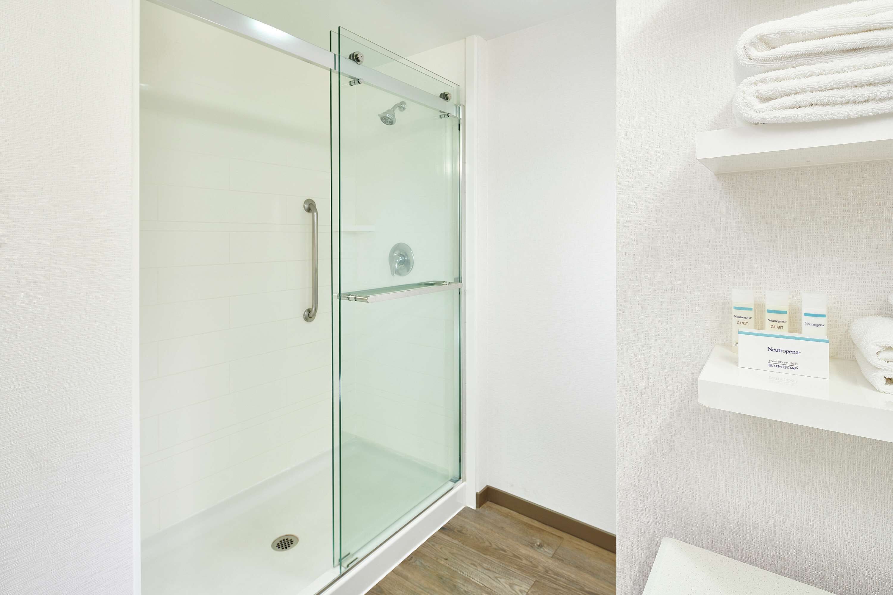 Een moderne badkamer met een douchecabine van glas, een witte wastafel en een plank met toiletartikelen.