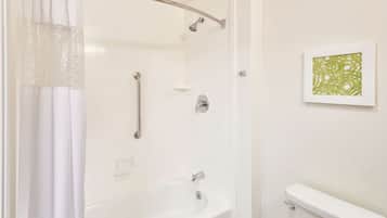 A bathroom with a bathtub, a toilet, a shower with a grab bar, and a framed artwork on the wall.