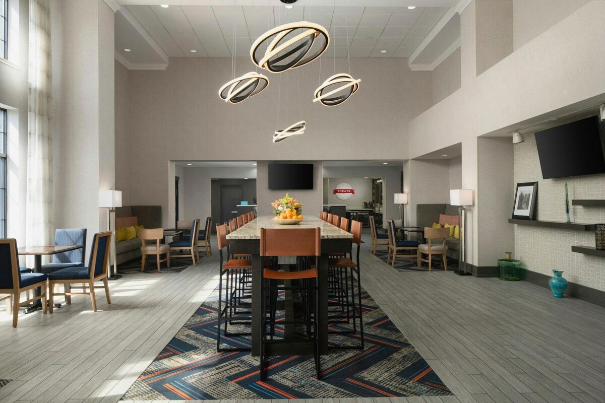 A spacious dining area with a long table, multiple chairs, and modern pendant lighting.