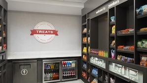 A store interior with shelves stocked with snacks and drinks, a refrigerated section, and a wall sign labeled "TREATS". - Hampton Inn & Suites Yonkers - Westchester (Yonkers)