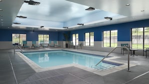 An indoor swimming pool with clear blue water, surrounded by lounge chairs and tables, and large windows offering views of the outdoors. - Hampton Inn & Suites Yonkers - Westchester (Yonkers)