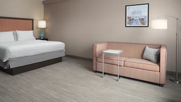 Quarto de hotel com cama, sofá, uma mesinha e duas luminárias.