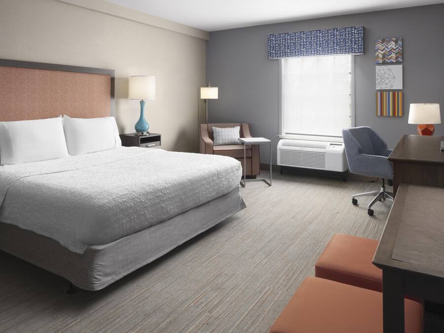 A hotel room with a large bed, a desk, a chair, a lamp, and a TV.
