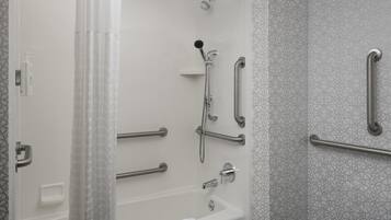 Un baño con ducha, barras de apoyo, toallero y soporte para papel higiénico.
