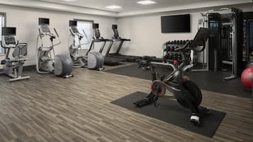 Un gimnasio con cintas de correr, elípticas, una bicicleta estática y equipo de levantamiento de pesas.