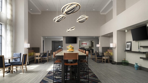 A spacious hotel dining area with a long table, multiple chairs, and modern pendant lighting. - Hampton Inn & Suites Yonkers - Westchester (Yonkers)