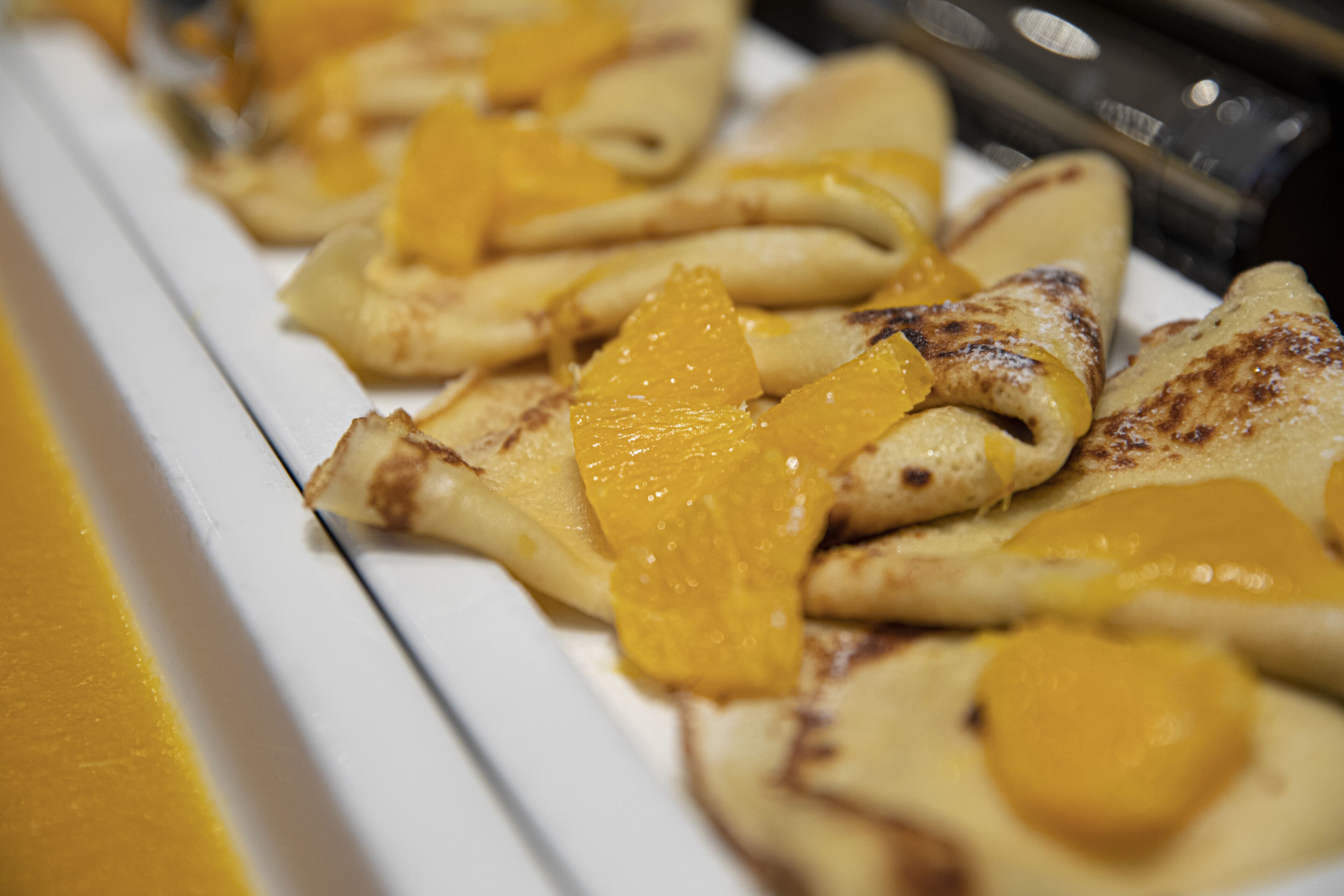 A plate of crepes with orange slices on a white plate.