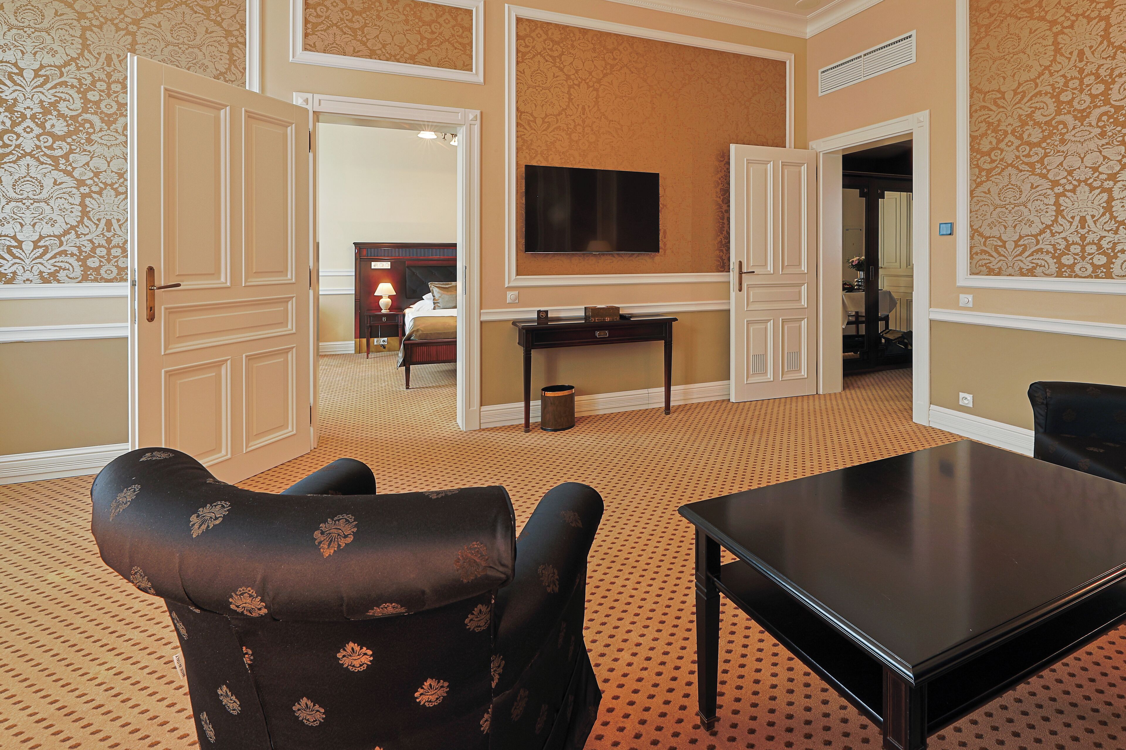A hotel room with a large bed, a TV mounted on the wall, a dining table, and a patterned carpet.