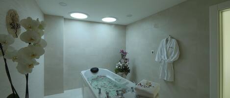 A modern bathroom with a freestanding bathtub, a white robe hanging on the wall, and a potted orchid plant.