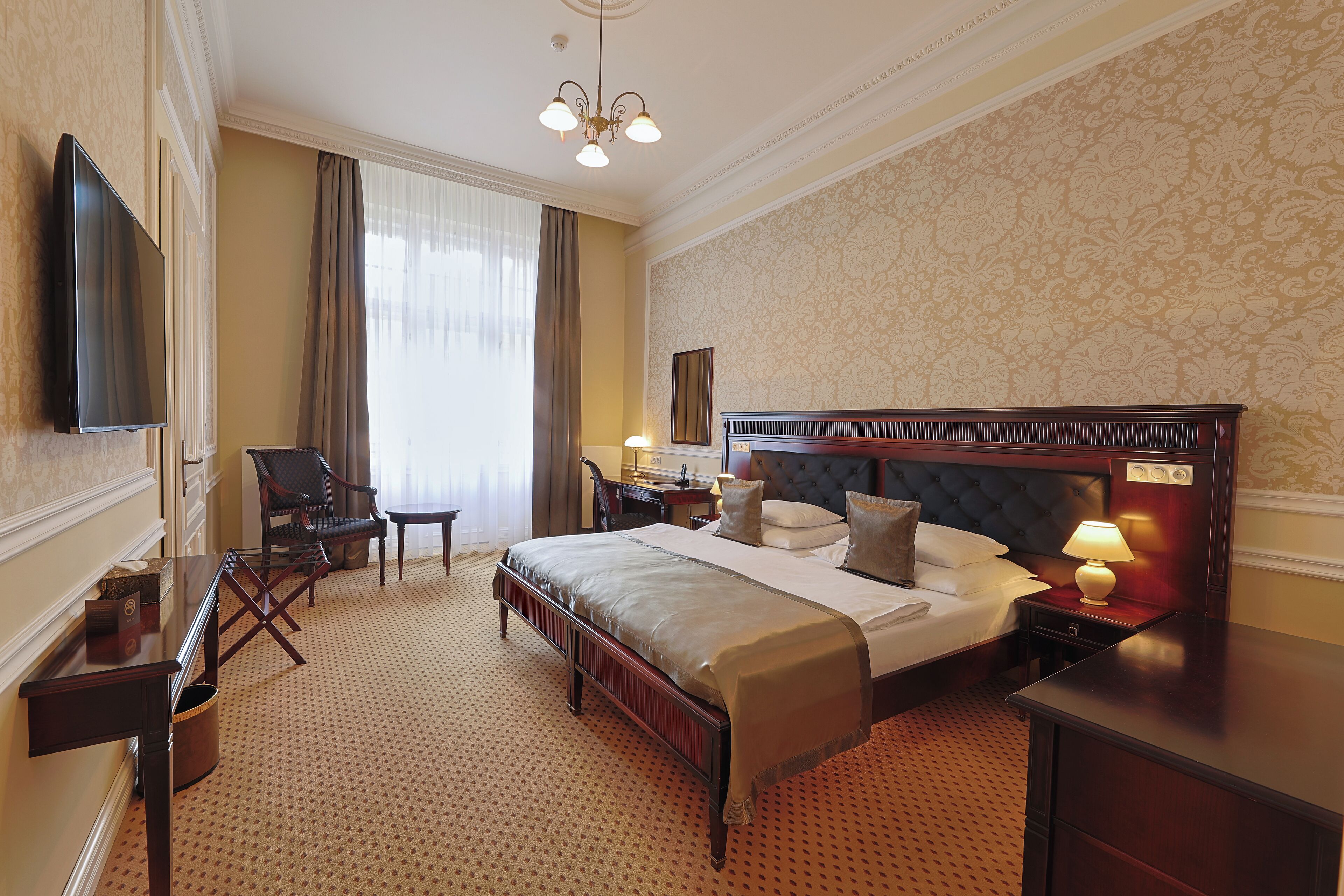 A hotel room with a large bed, a desk, a chair, a television, and a lamp.