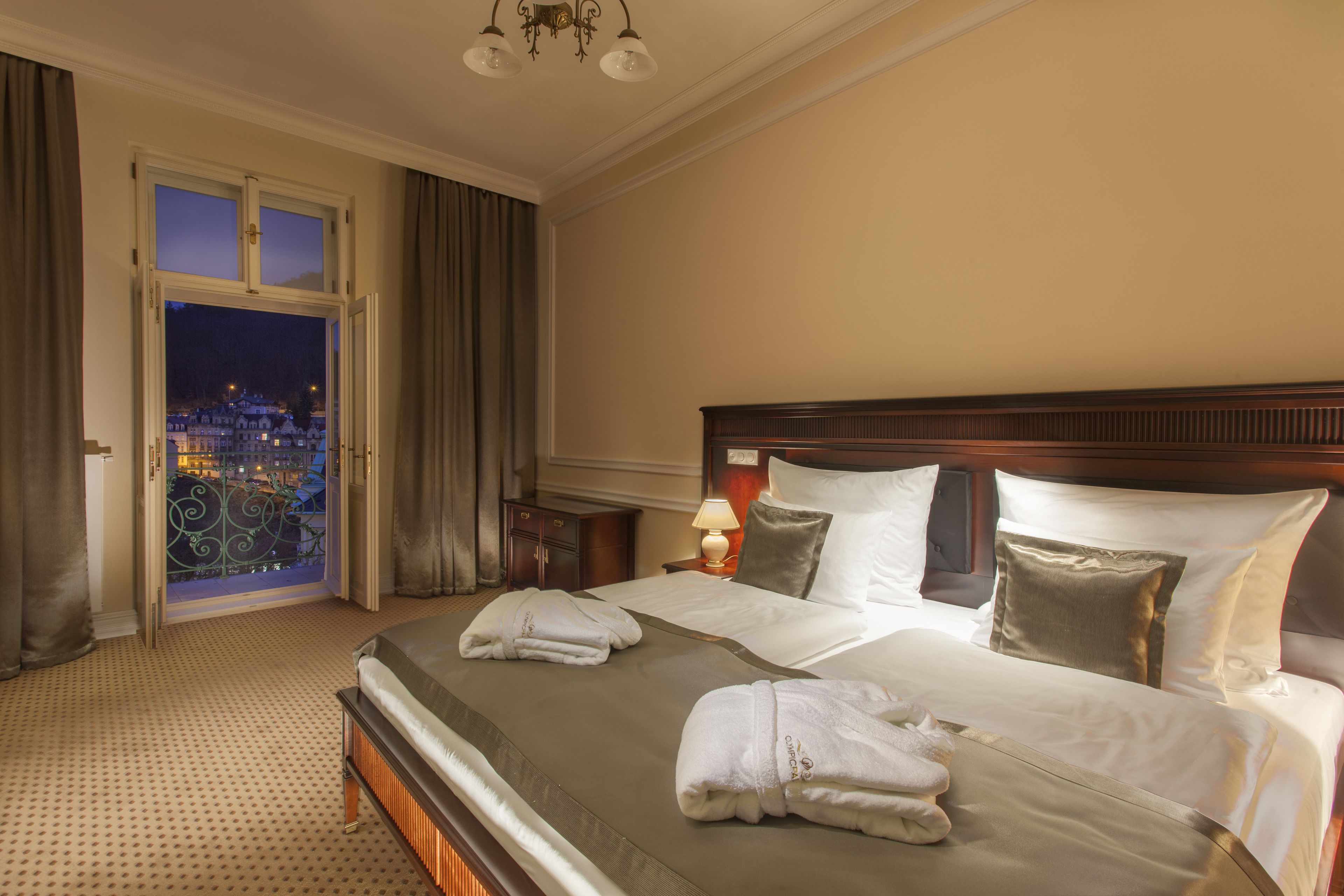 Une chambre d’hôtel avec un grand lit, une table de chevet, une lampe et une vue sur la ville la nuit.