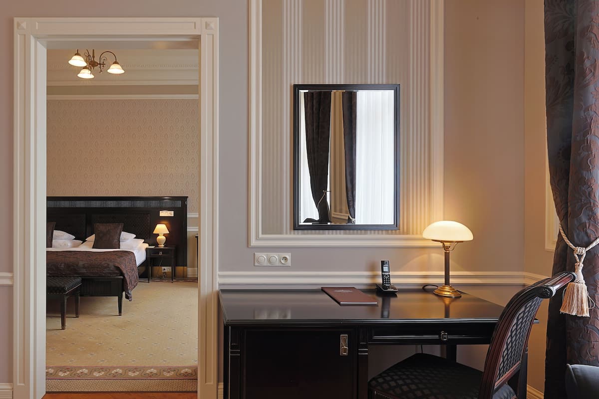 A hotel room with a bed, bedside table, lamp, and a desk with a chair.