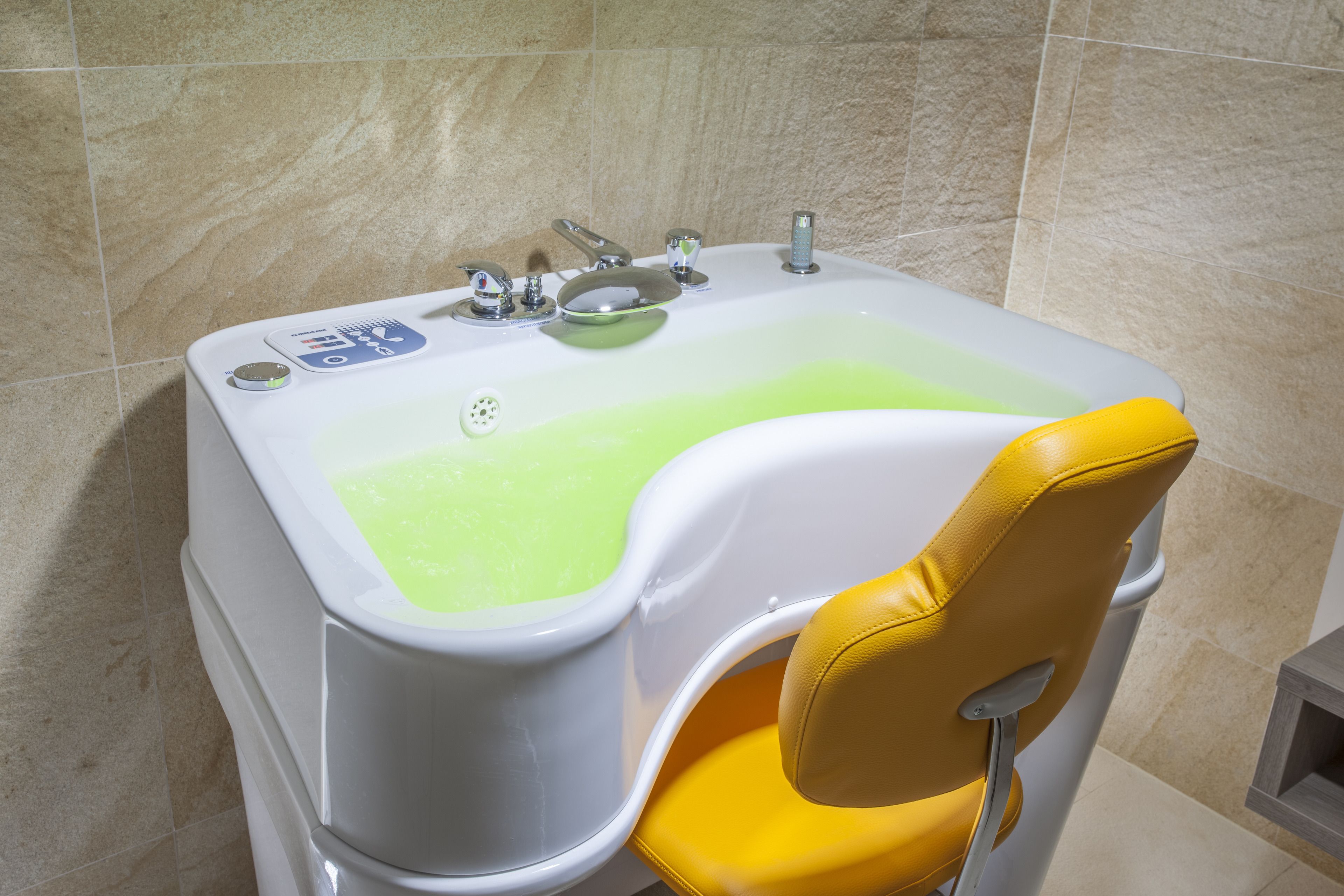 A bathtub with a yellow chair, a control panel, and a green water feature.