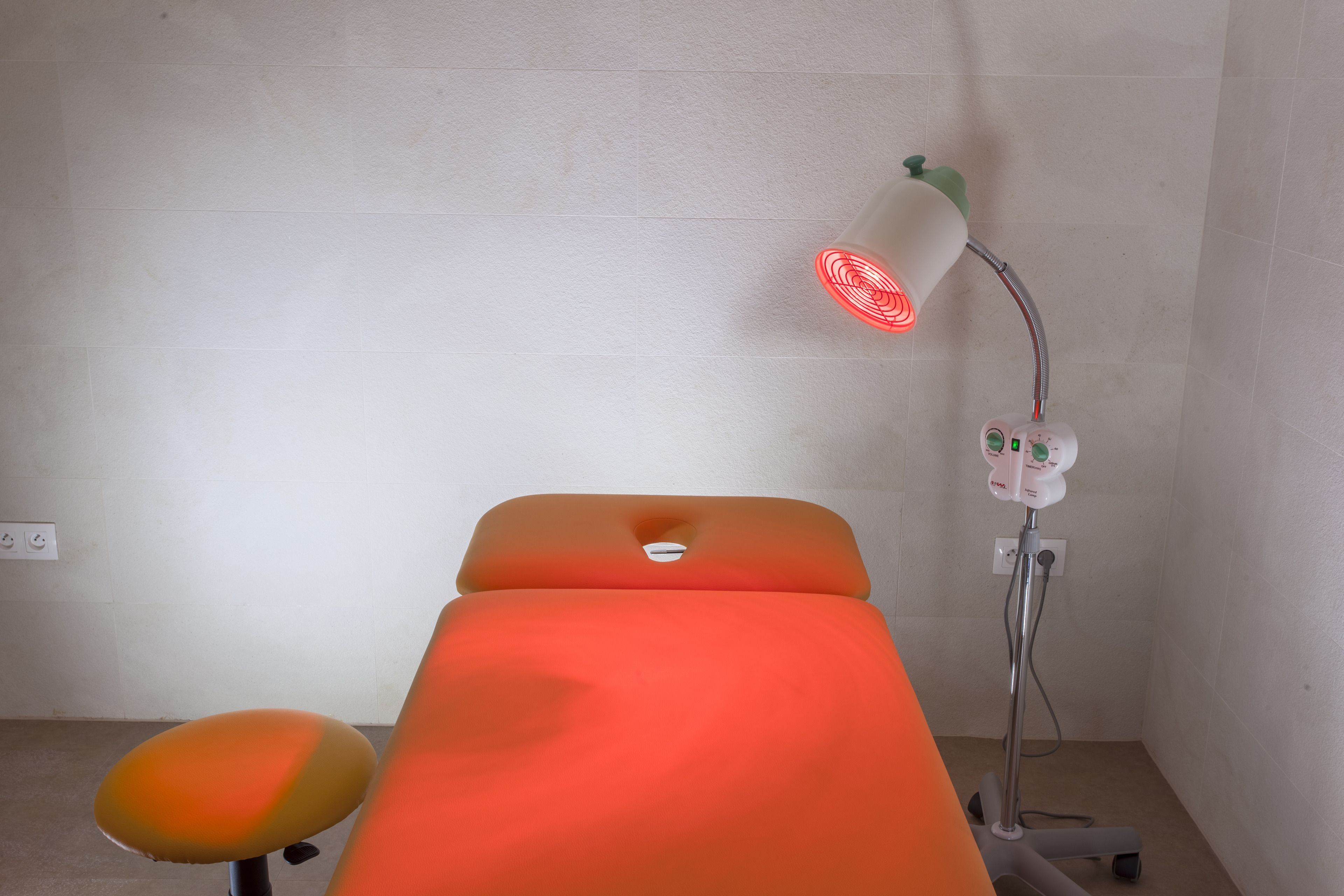 A medical examination table with a red light, a chair, and a foot massager.