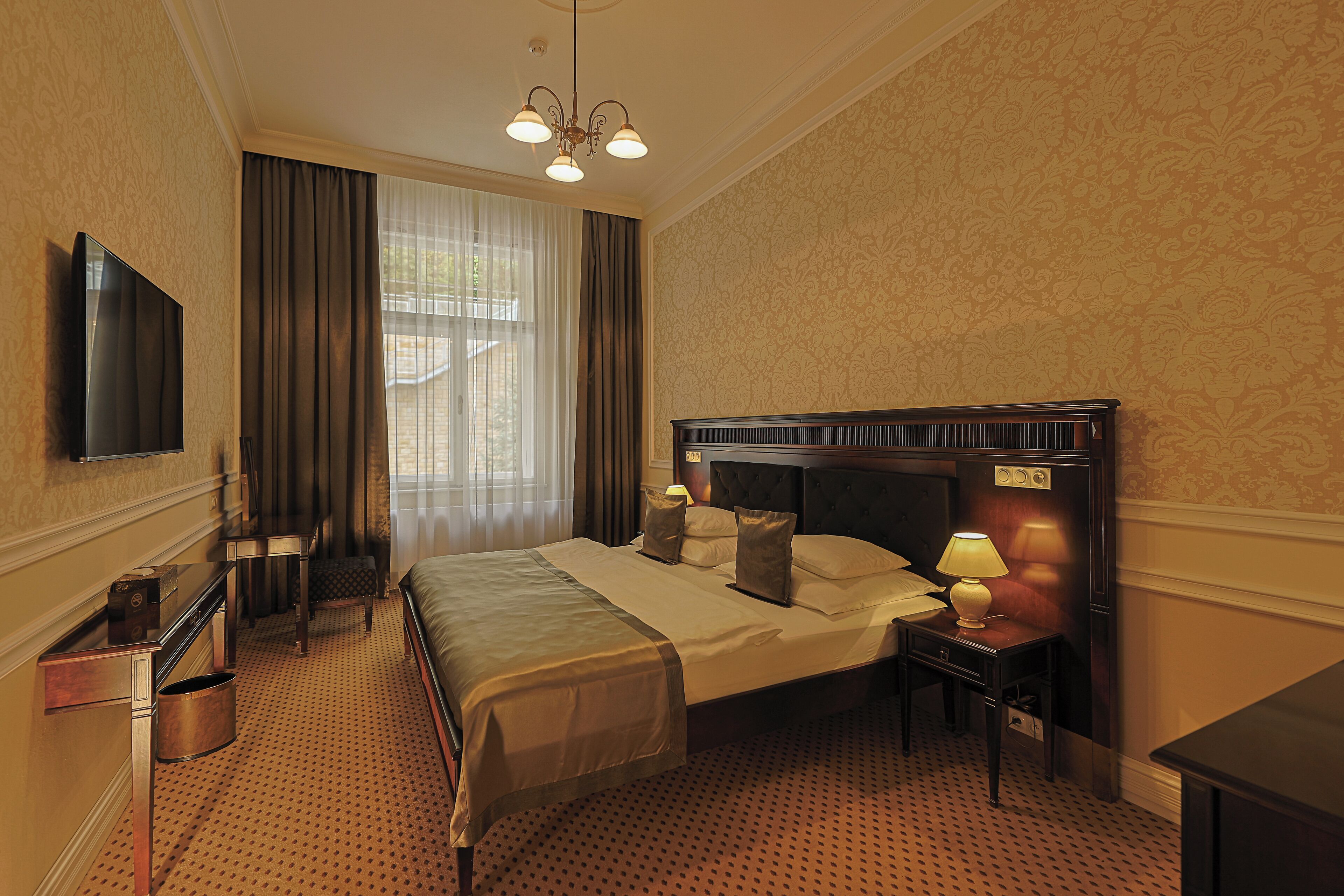 A hotel room with a large bed, a desk, a chair, a television, and a lamp.