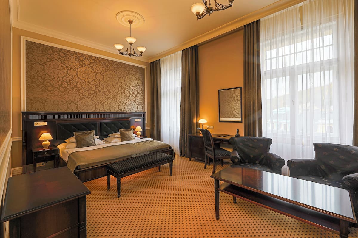 A hotel room with a large bed, a desk, a chair, a sofa, and a chandelier.