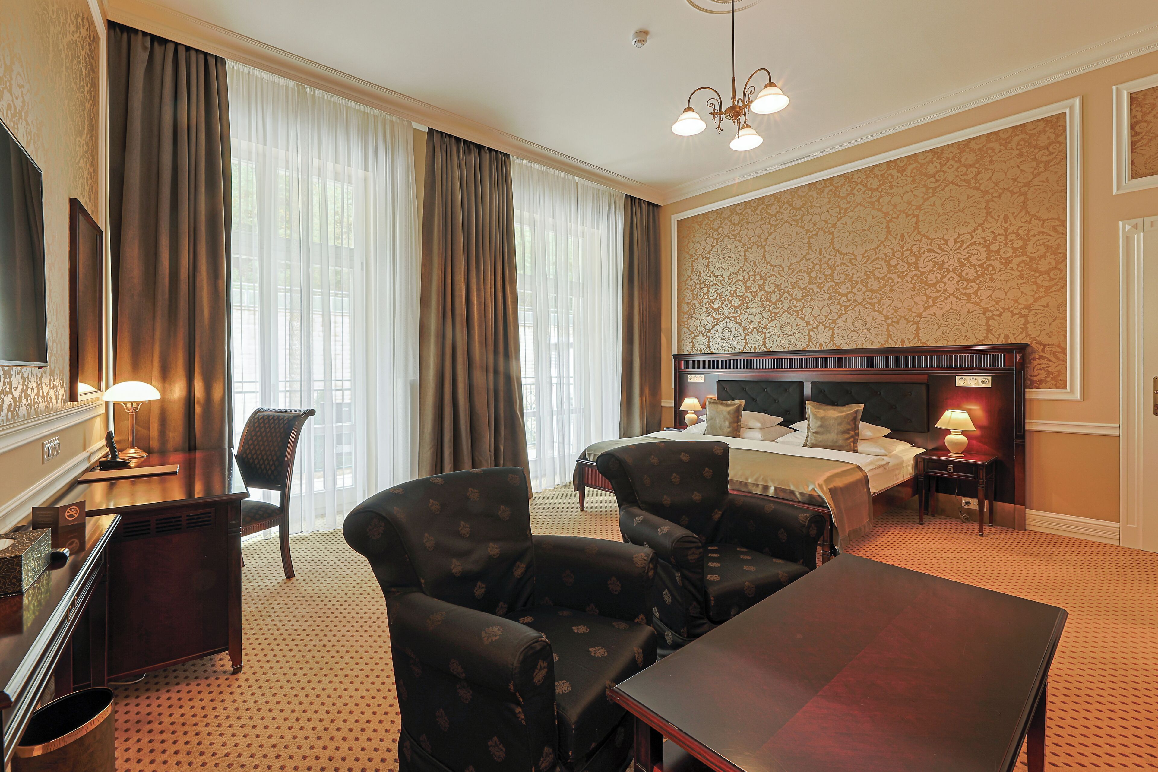 A hotel room with a bed, two armchairs, a desk, and a TV.