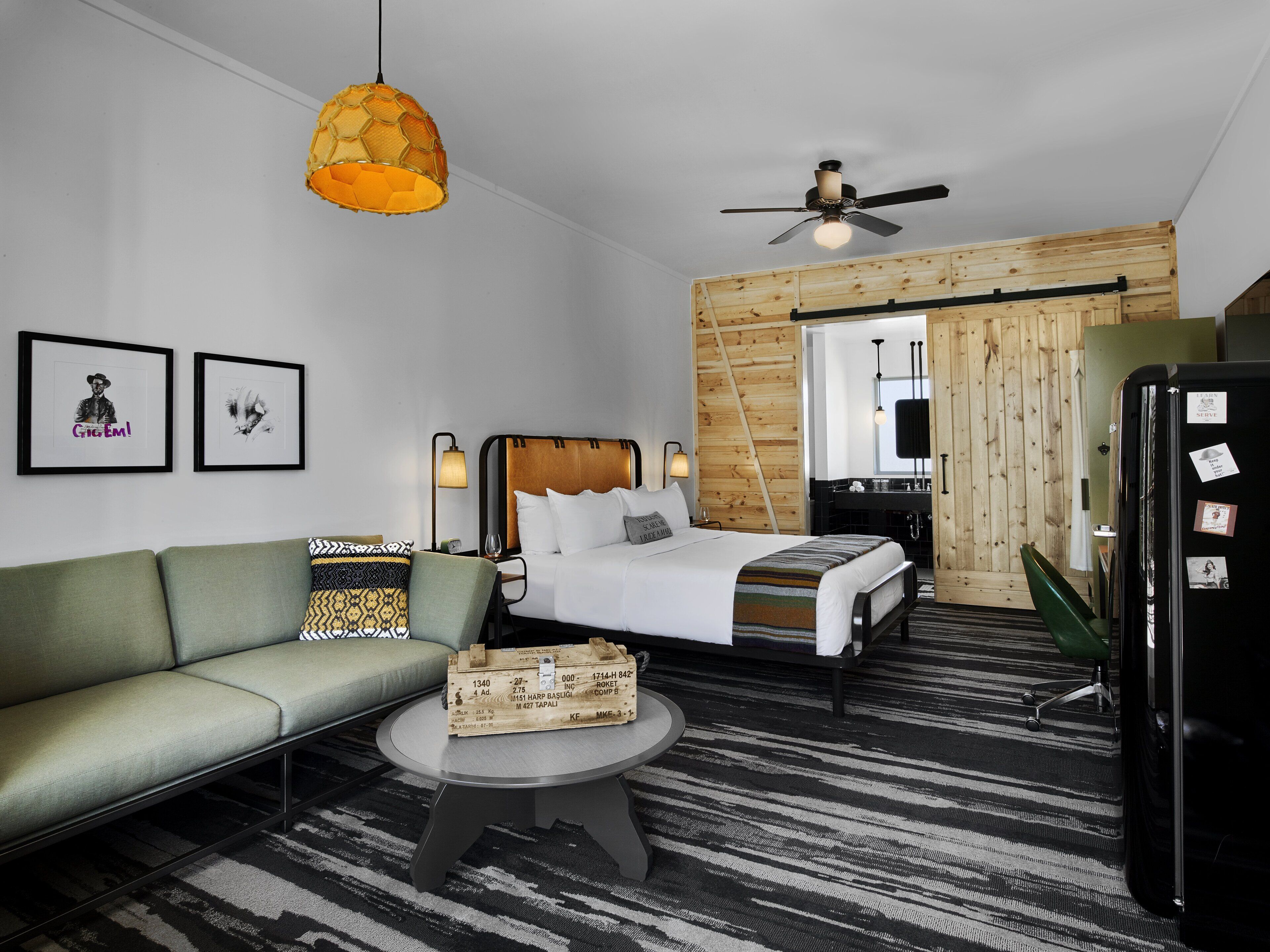 Una habitación de hotel moderna con cama, sofá, mesa de centro, ventilador de techo y refrigerador.