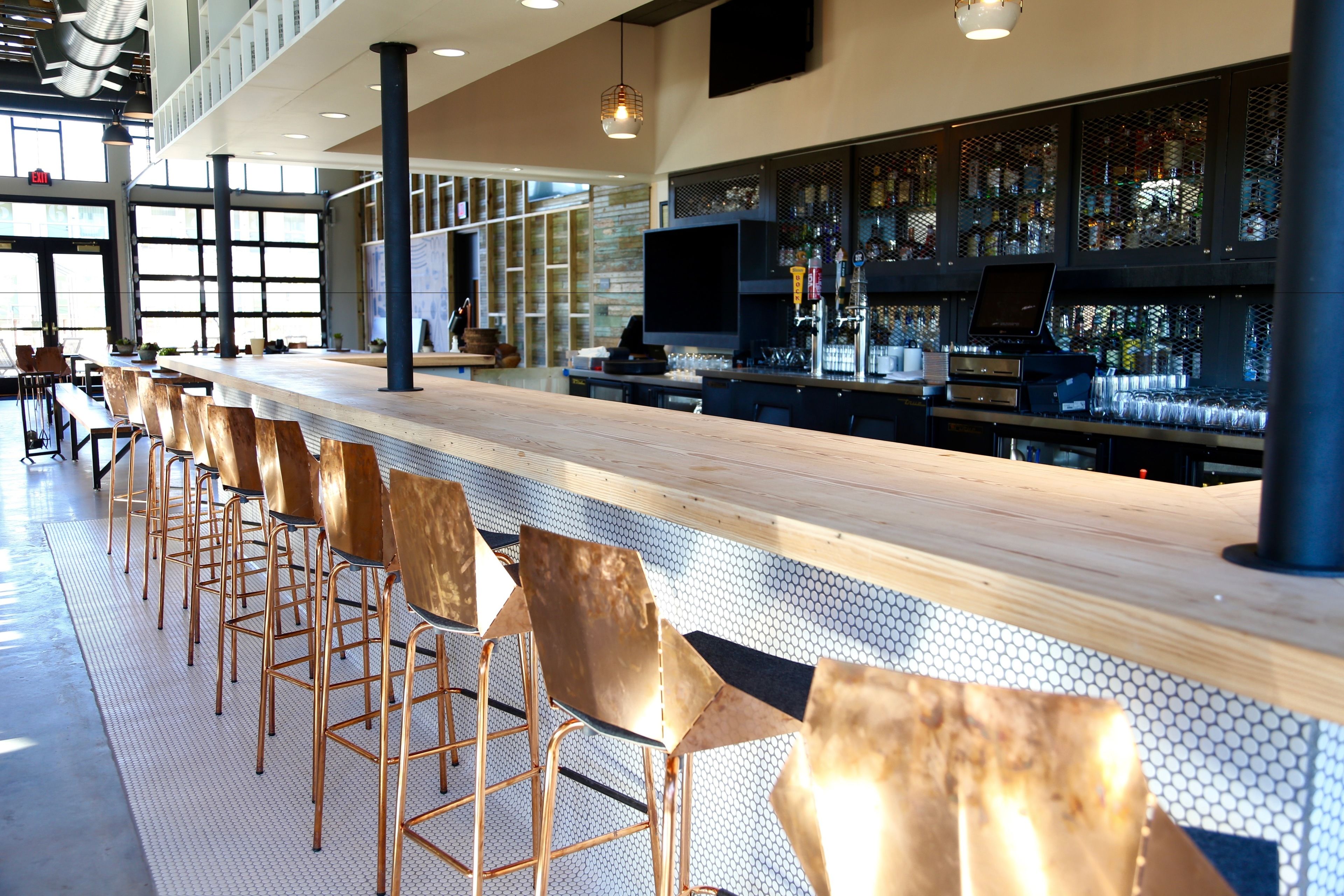 A bar area with a long wooden counter, multiple bar stools, and a television screen.