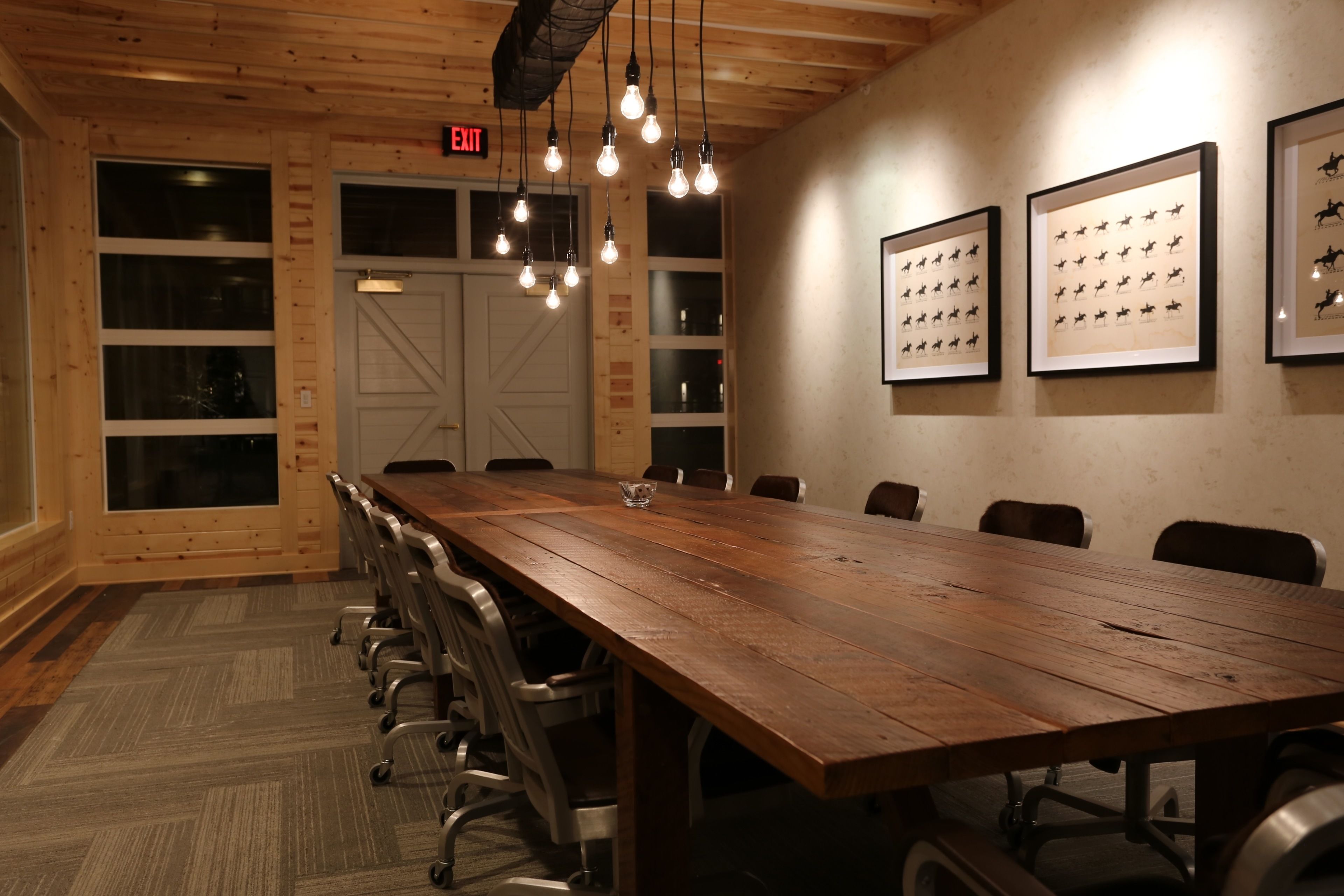 A conference room with a long wooden table, chairs, and framed horse silhouettes on the wall.