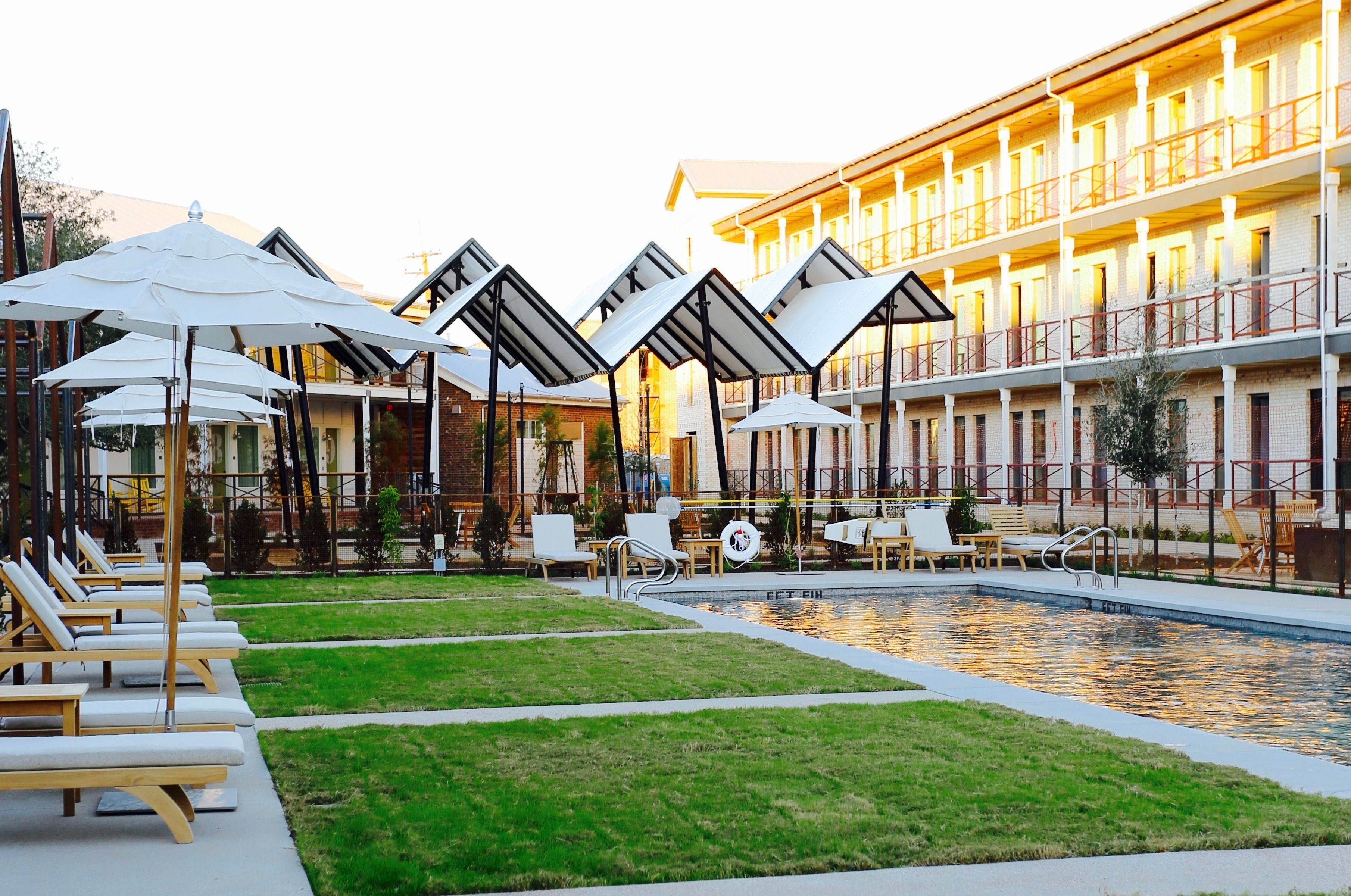 A hotel with a swimming pool, outdoor seating, and a covered area with umbrellas.