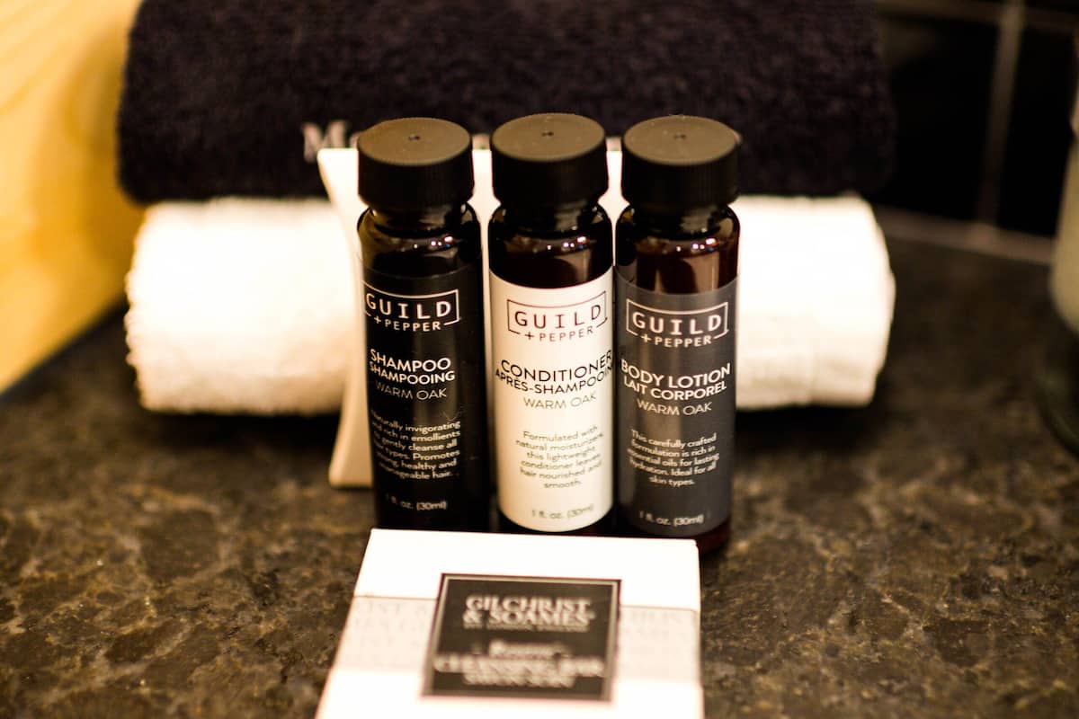 A bathroom counter with three bottles of Guild Pepper shampoo and conditioner, and a box of body lotion.