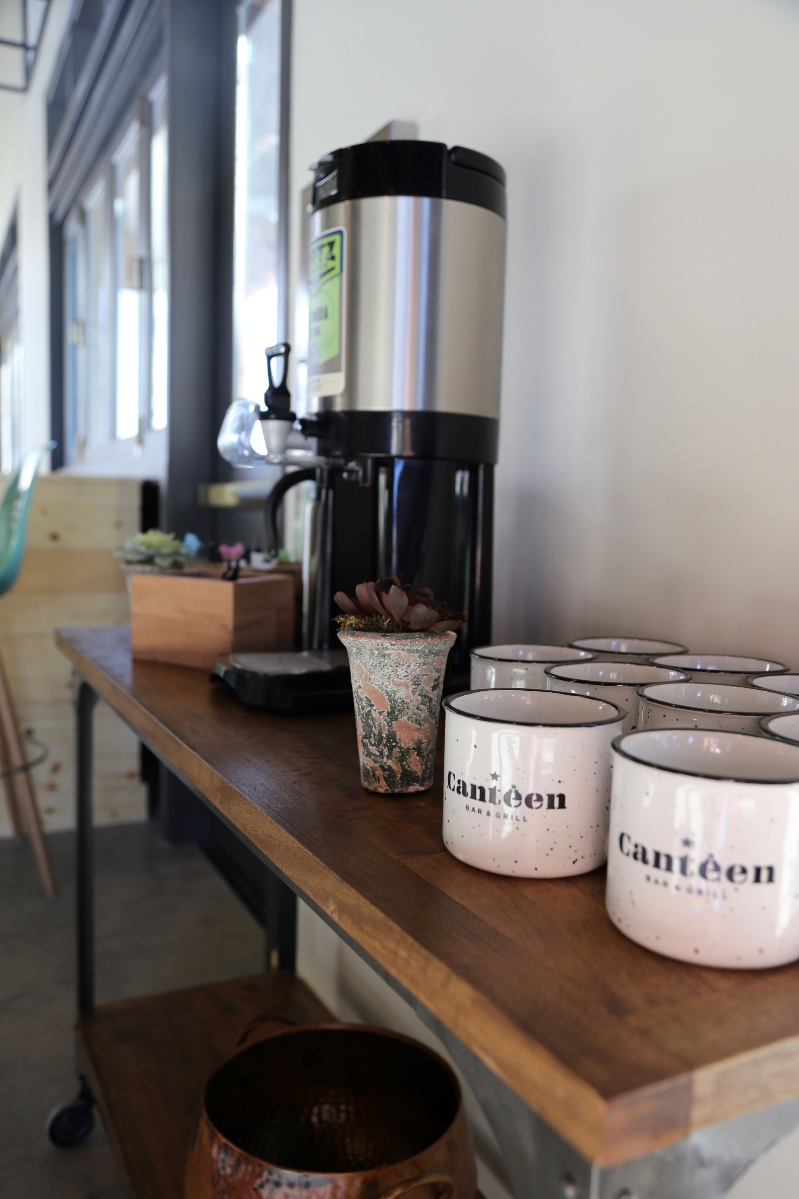 A coffee machine, a planter, and several mugs on a wooden table.