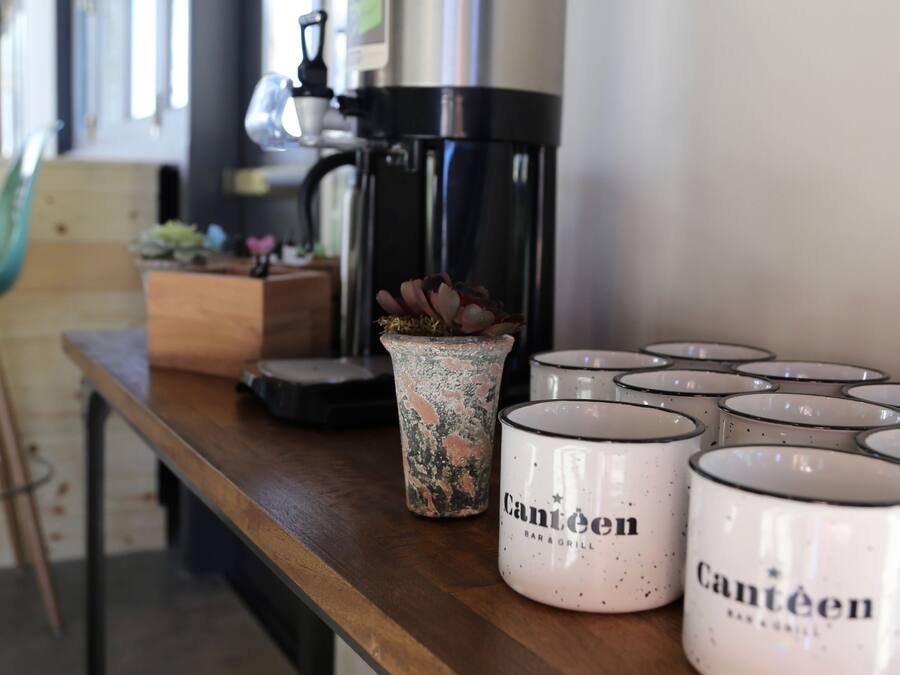 Una cafetera, una maceta y varias tazas sobre una mesa de madera.