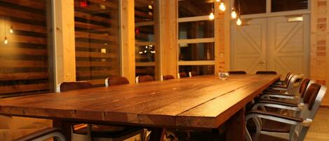 Una larga mesa de conferencias de madera con sillas metálicas, ubicada en una habitación con paredes de madera y ventanas amplias.