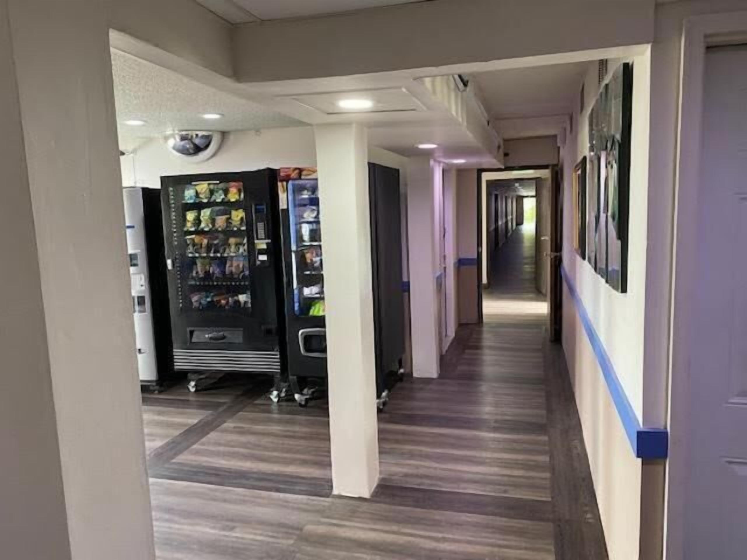 A hallway with a vending machine, wooden flooring, and a door on the right.