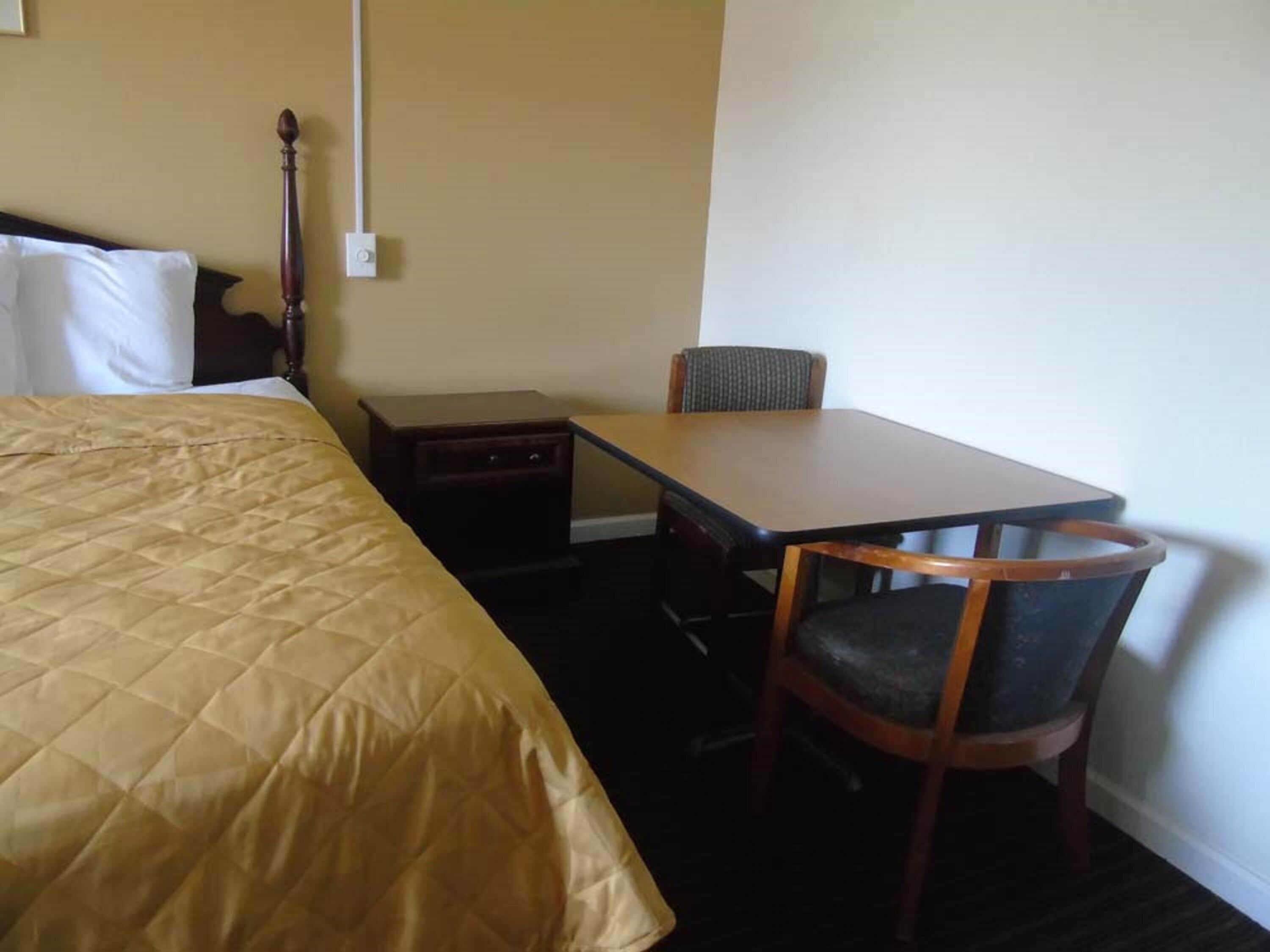 A hotel room with a bed, a small table, a chair, and a nightstand.