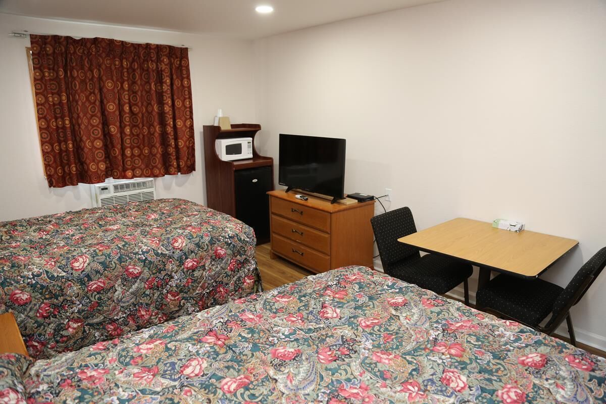 A room with two beds, a desk, a chair, a television, and a microwave.