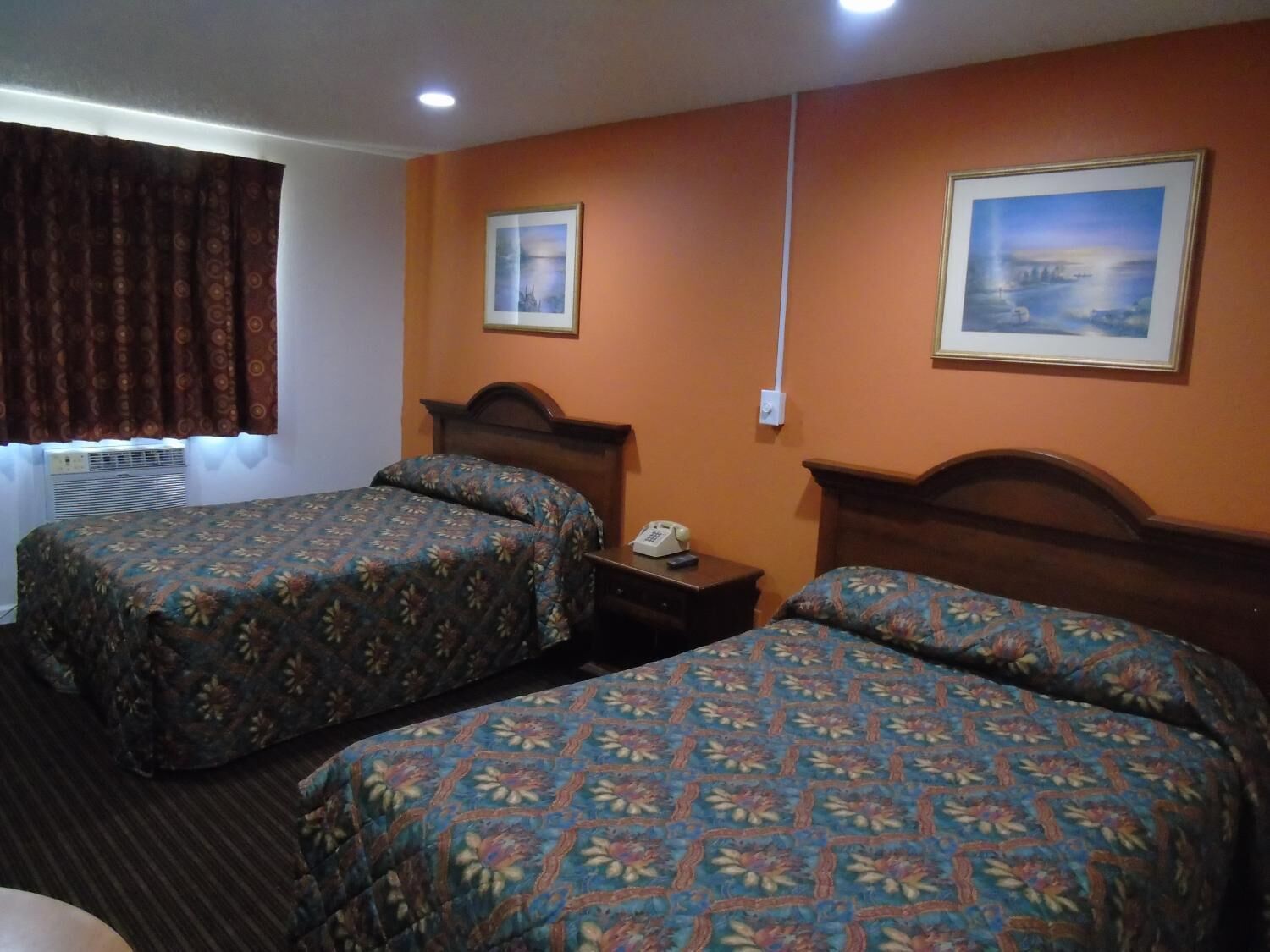 Habitación de hotel con dos camas, una mesita de noche, un teléfono y dos cuadros en la pared.