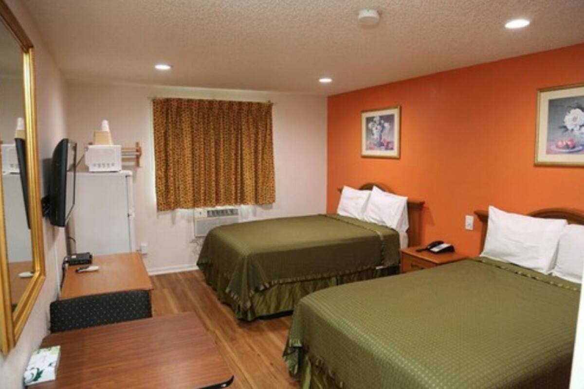 A hotel room with two single beds, a desk, a chair, a TV, and a window with curtains.