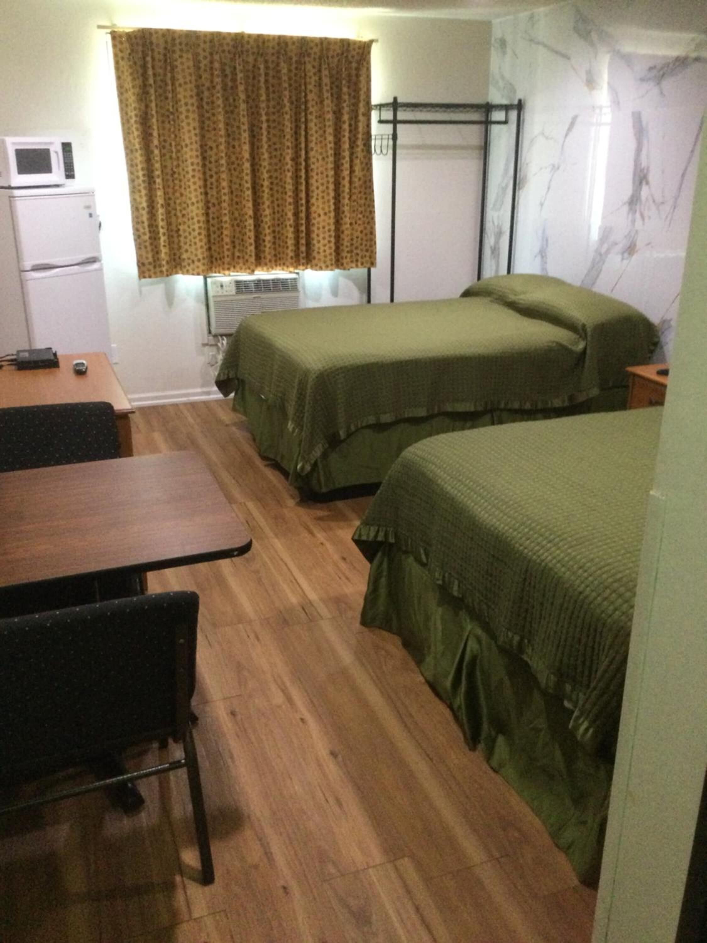 A small, compact room with two single beds, a wooden table, a chair, a microwave, and a small refrigerator.