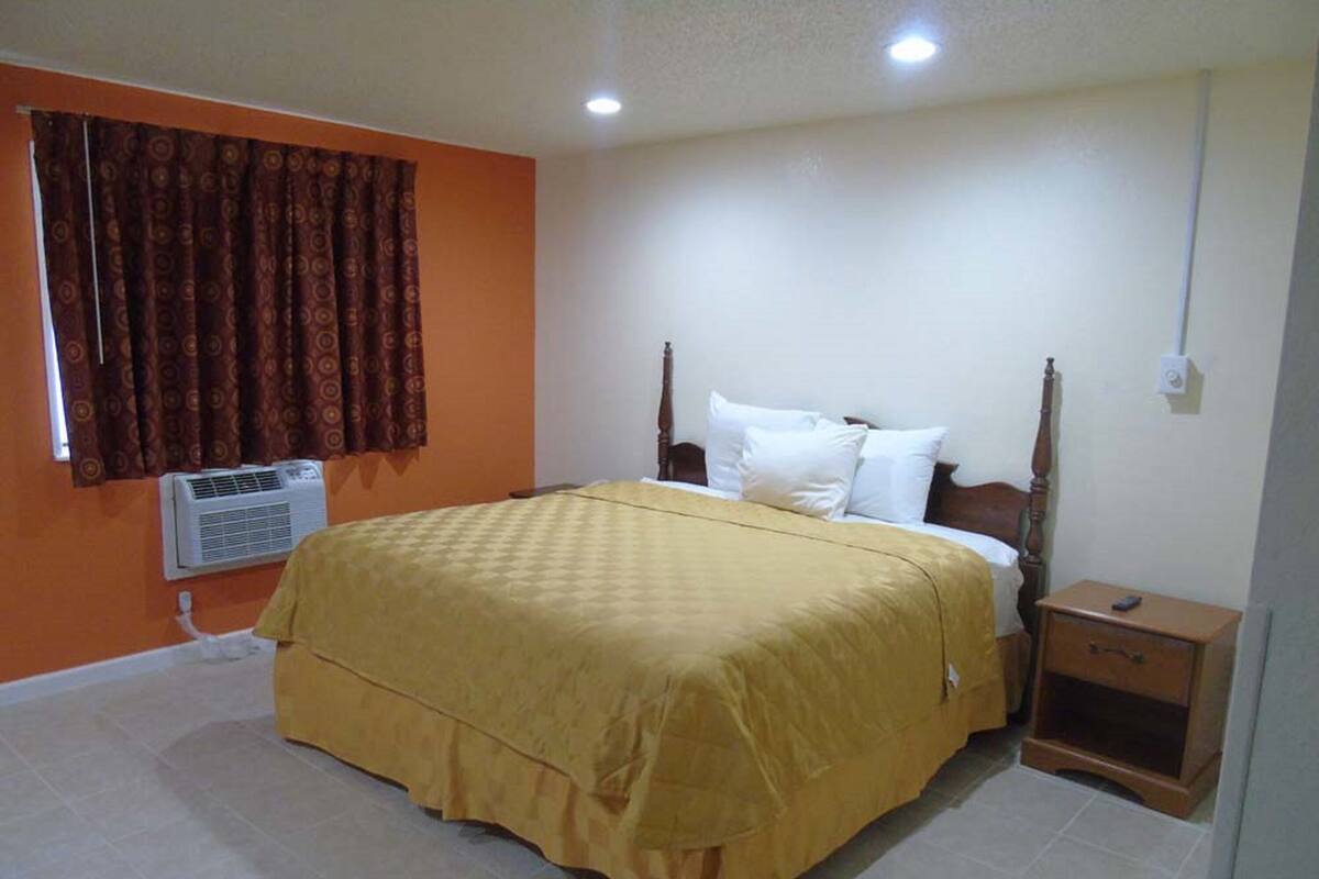 A bedroom with a bed, a nightstand, an air conditioning unit, and a window with curtains.
