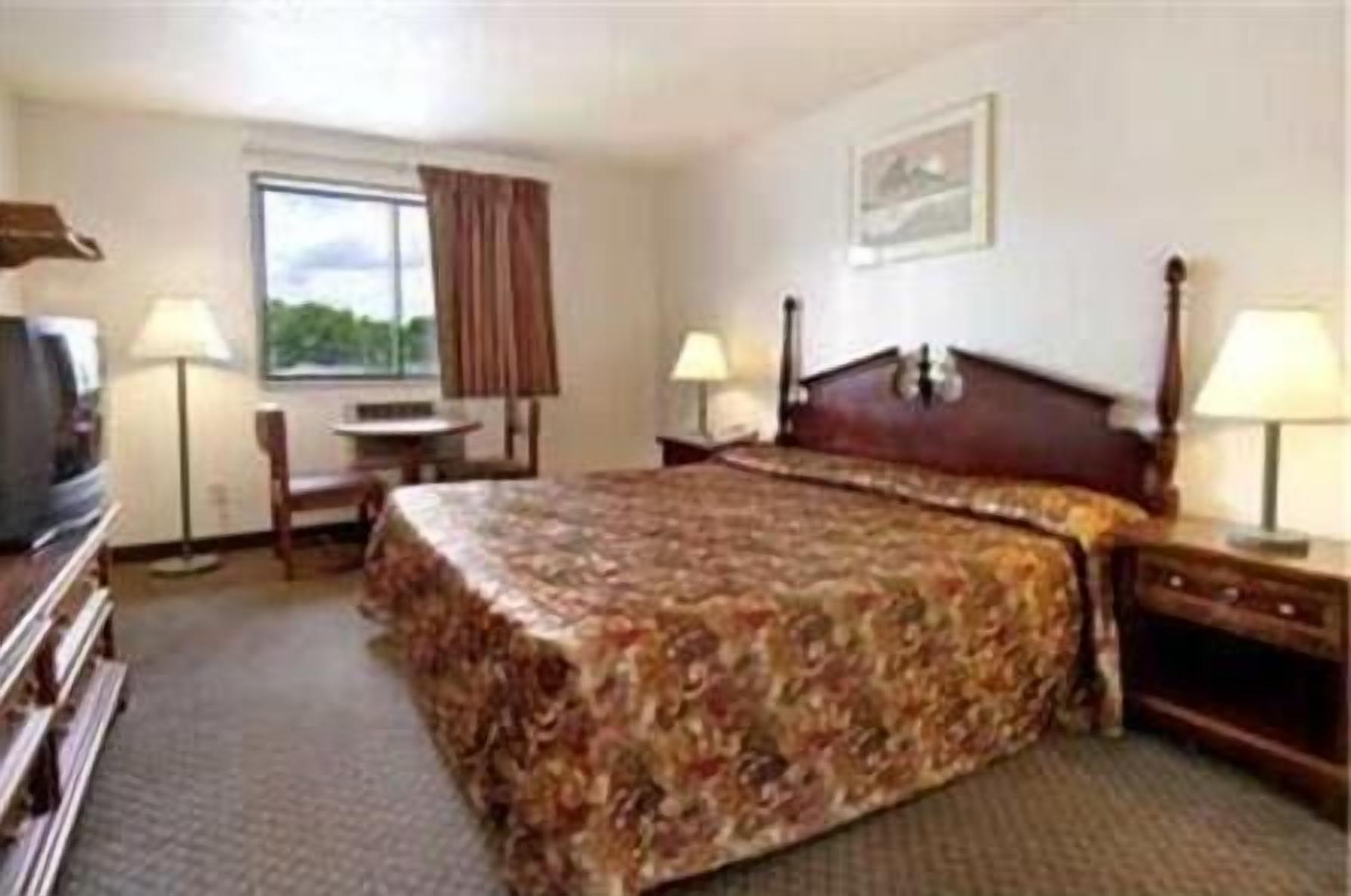 A hotel room with a bed, a desk, a chair, a television, and two lamps.