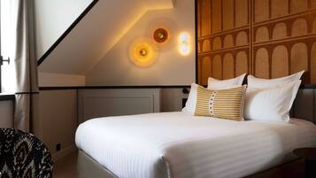 A neatly made bed with white linens and striped pillows, a wooden headboard, and a wall with a geometric pattern.