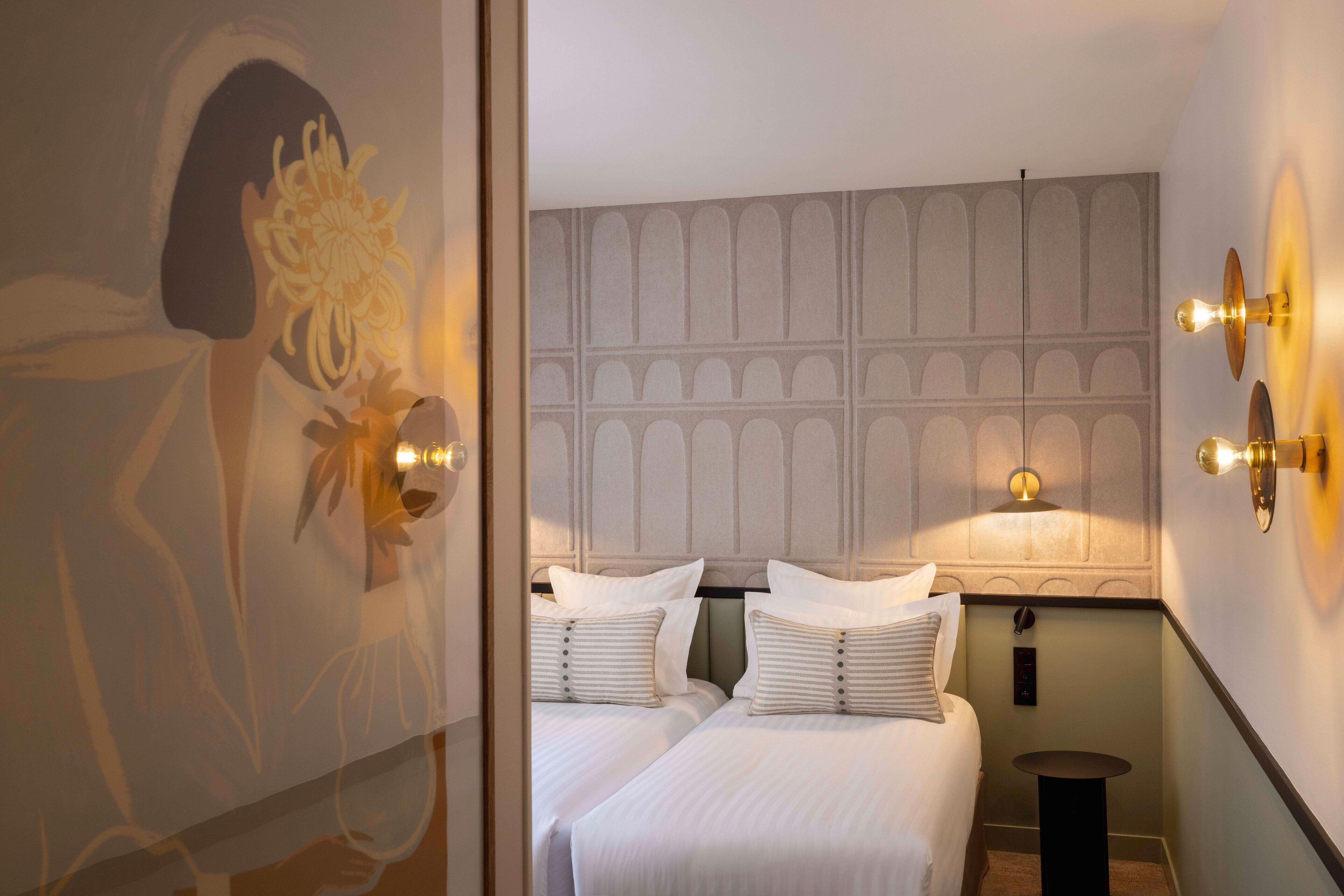 A hotel room with two beds, a decorative wall panel, and wall-mounted lights.