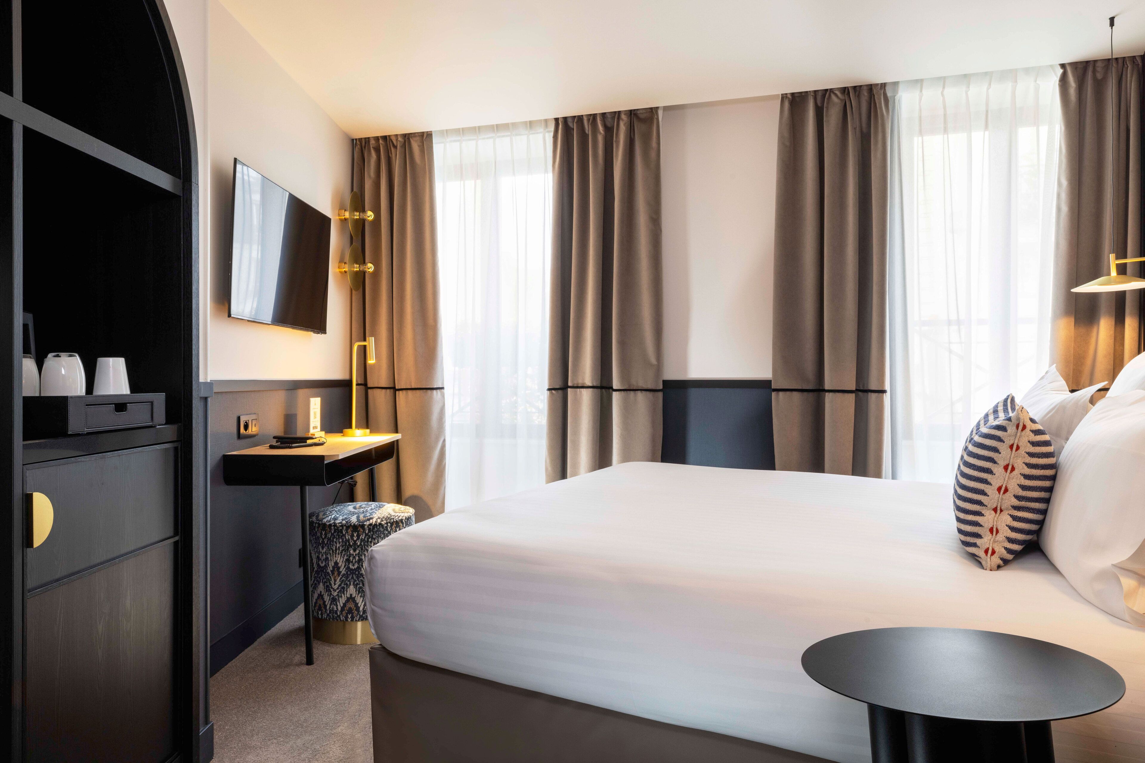 A hotel room with a large bed, a desk with a lamp, a TV, and a small round table.
