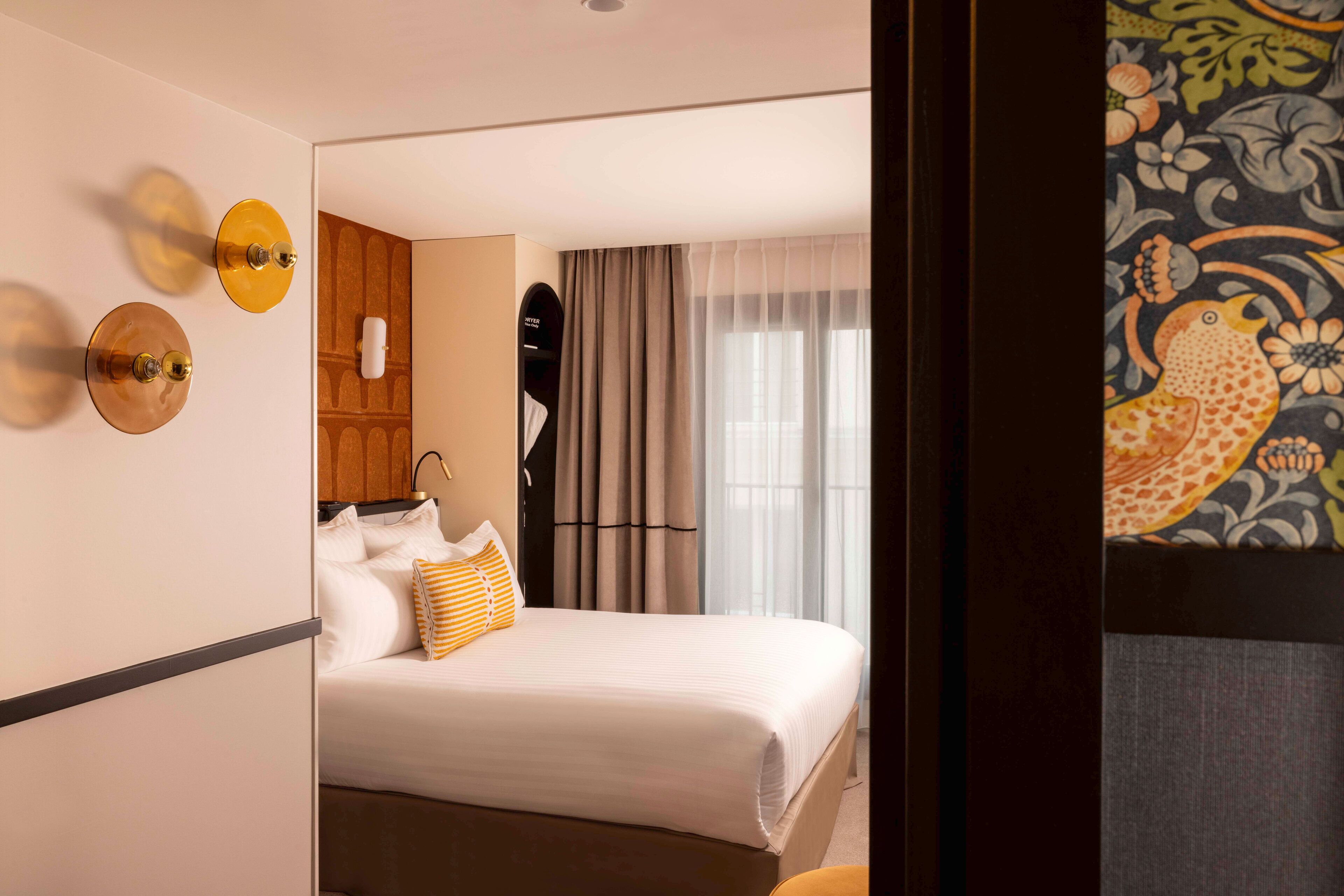 Una camera d'albergo con un letto, uno specchio, un armadio e una finestra con tende.