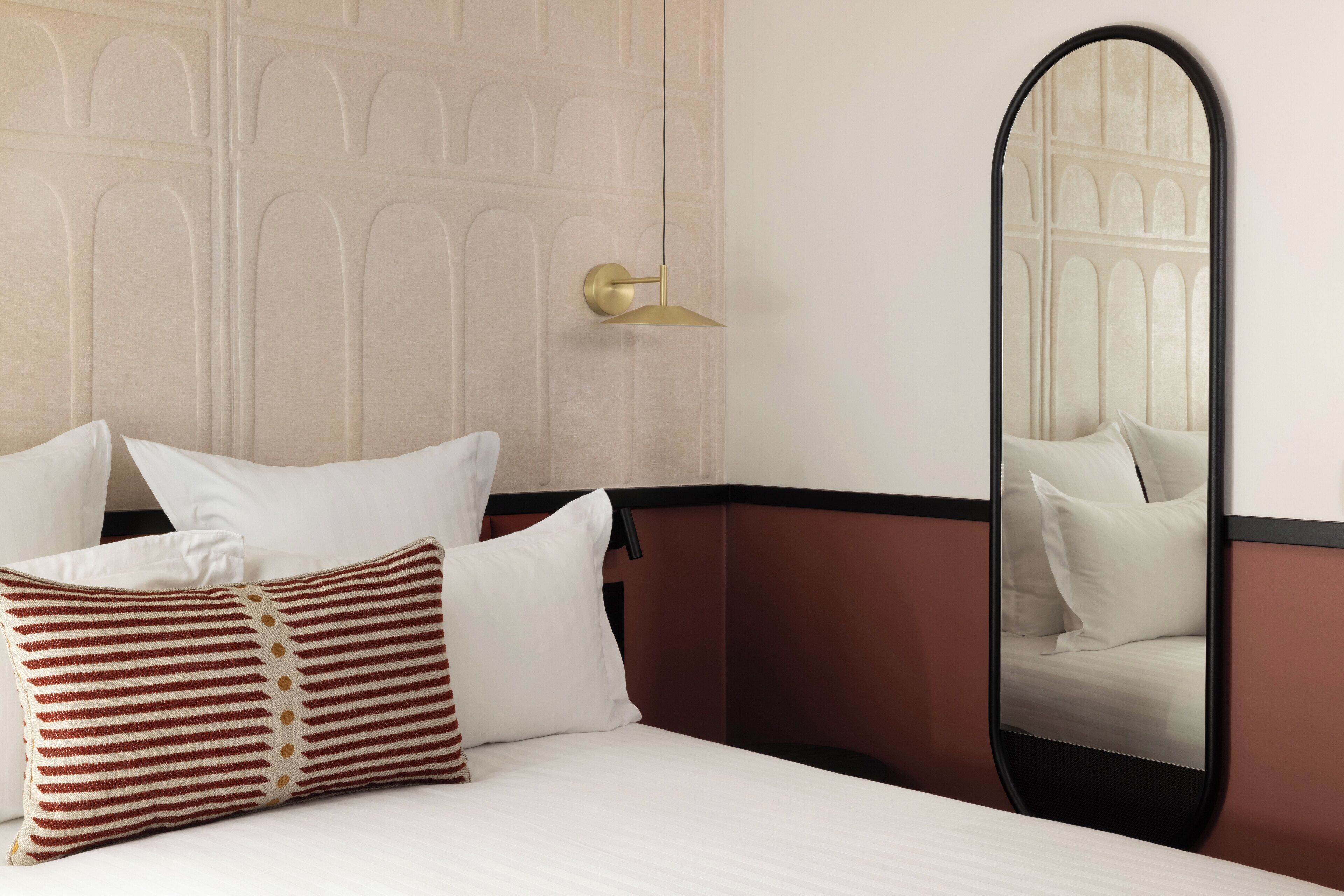 Habitación de hotel con cama, almohadas, un espejo y una puerta con picaporte de latón.