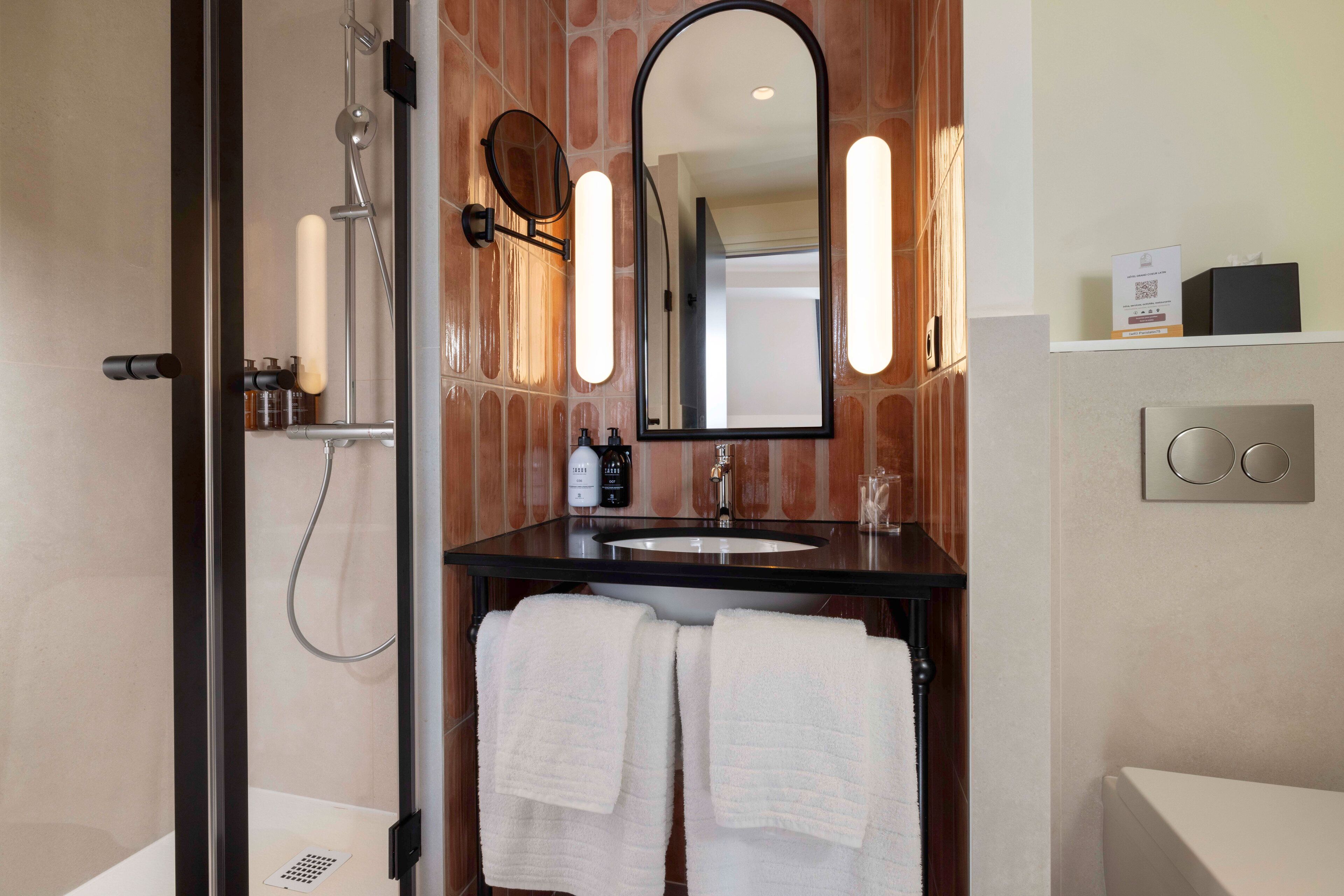 A modern bathroom with a glass-enclosed shower, a black sink, and a large mirror with wall-mounted lights.