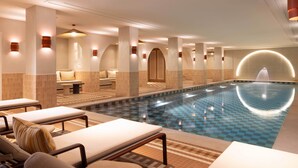 A large indoor swimming pool with lounge chairs and a fountain.