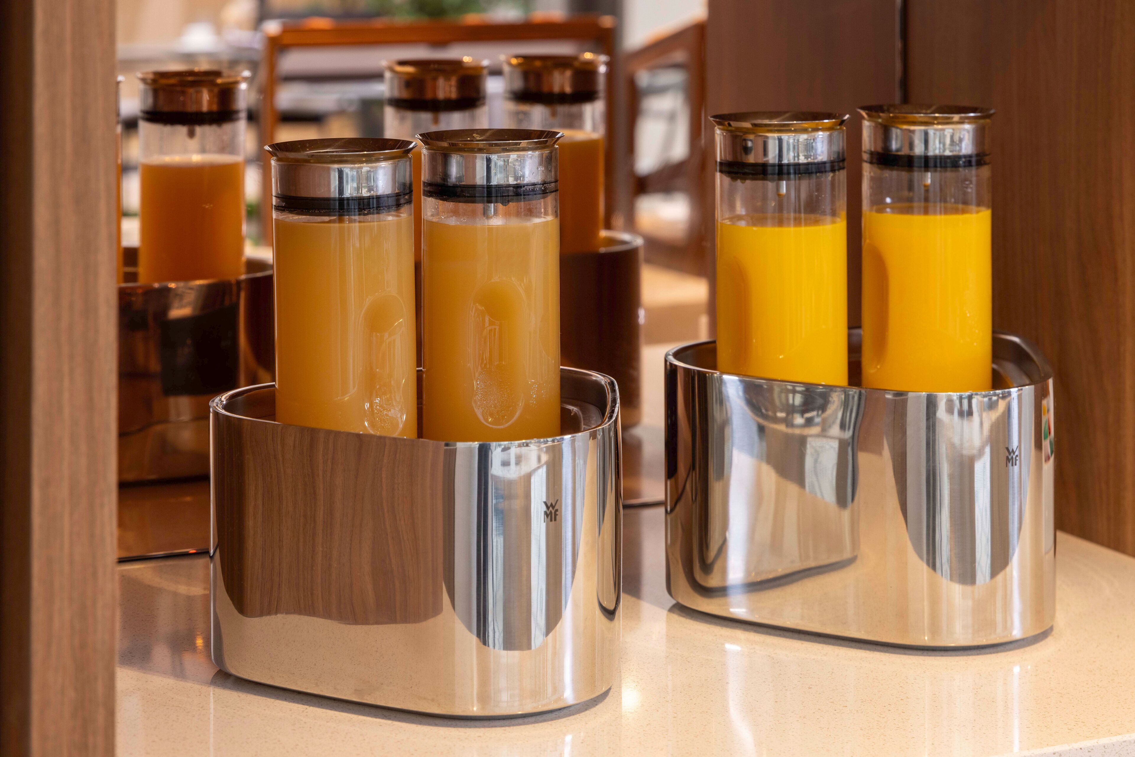 Un comptoir de petit-déjeuner doté de plusieurs distributeurs en acier inoxydable contenant du jus d’orange.