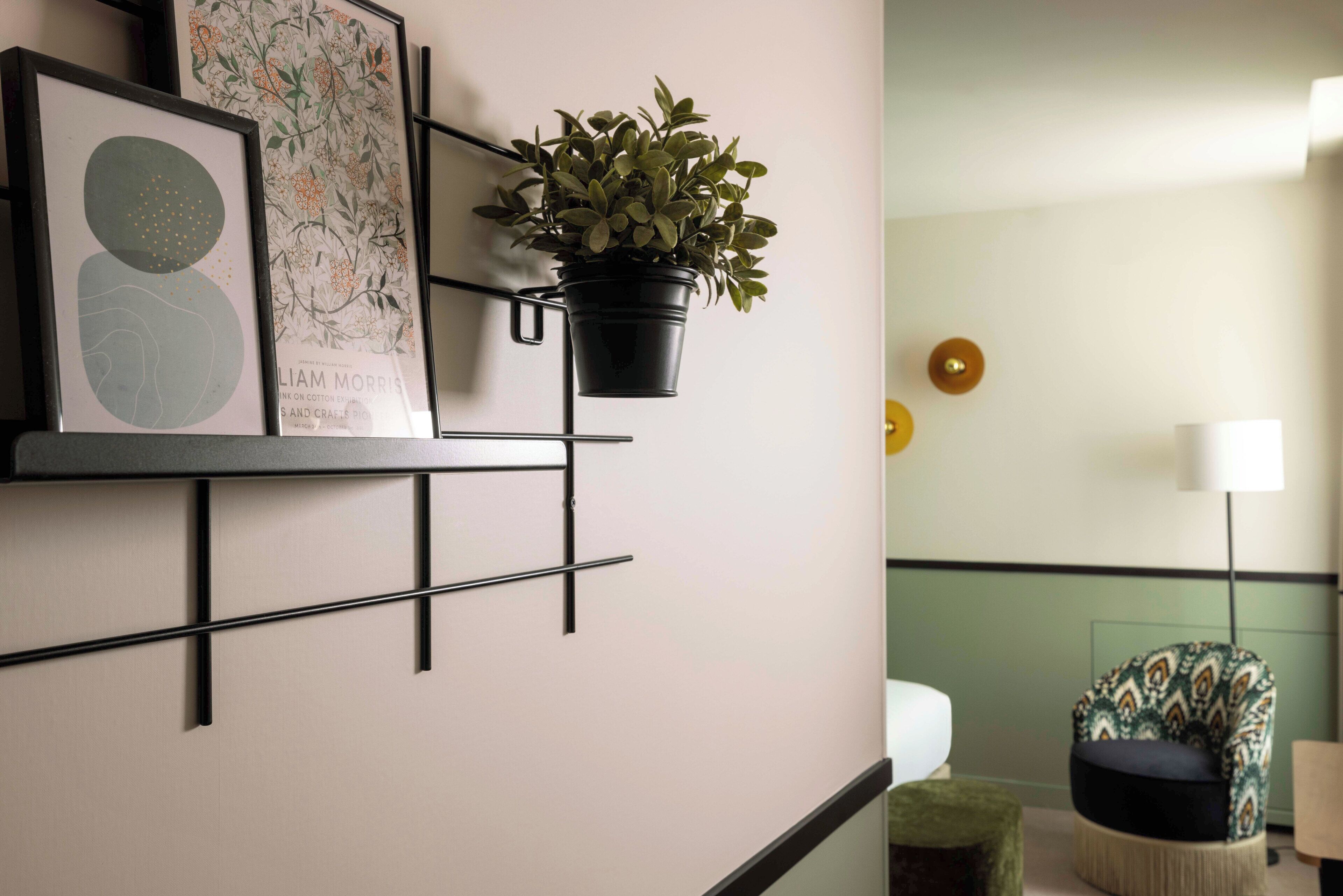 A modern room with a minimalist design, featuring a wall-mounted shelf with framed artwork and a potted plant.